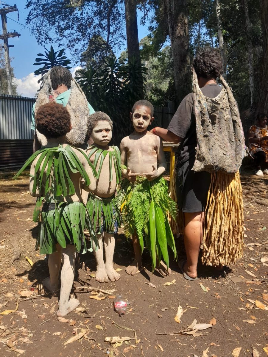 Children in leaf bilas, seen from behind with bilum bags